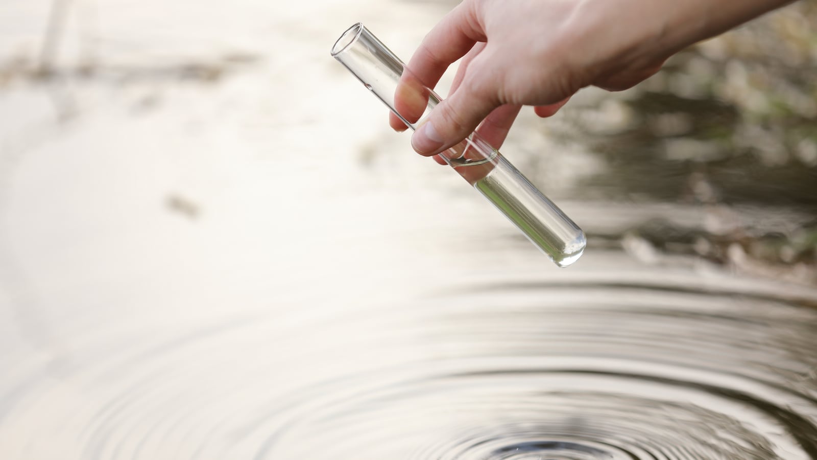 Illustrative hand holding a test tube to collect a water sample